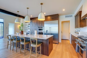Una cocina moderna con una isla central, taburetes de bar, iluminación colgante, electrodomésticos de acero inoxidable y armarios de madera.