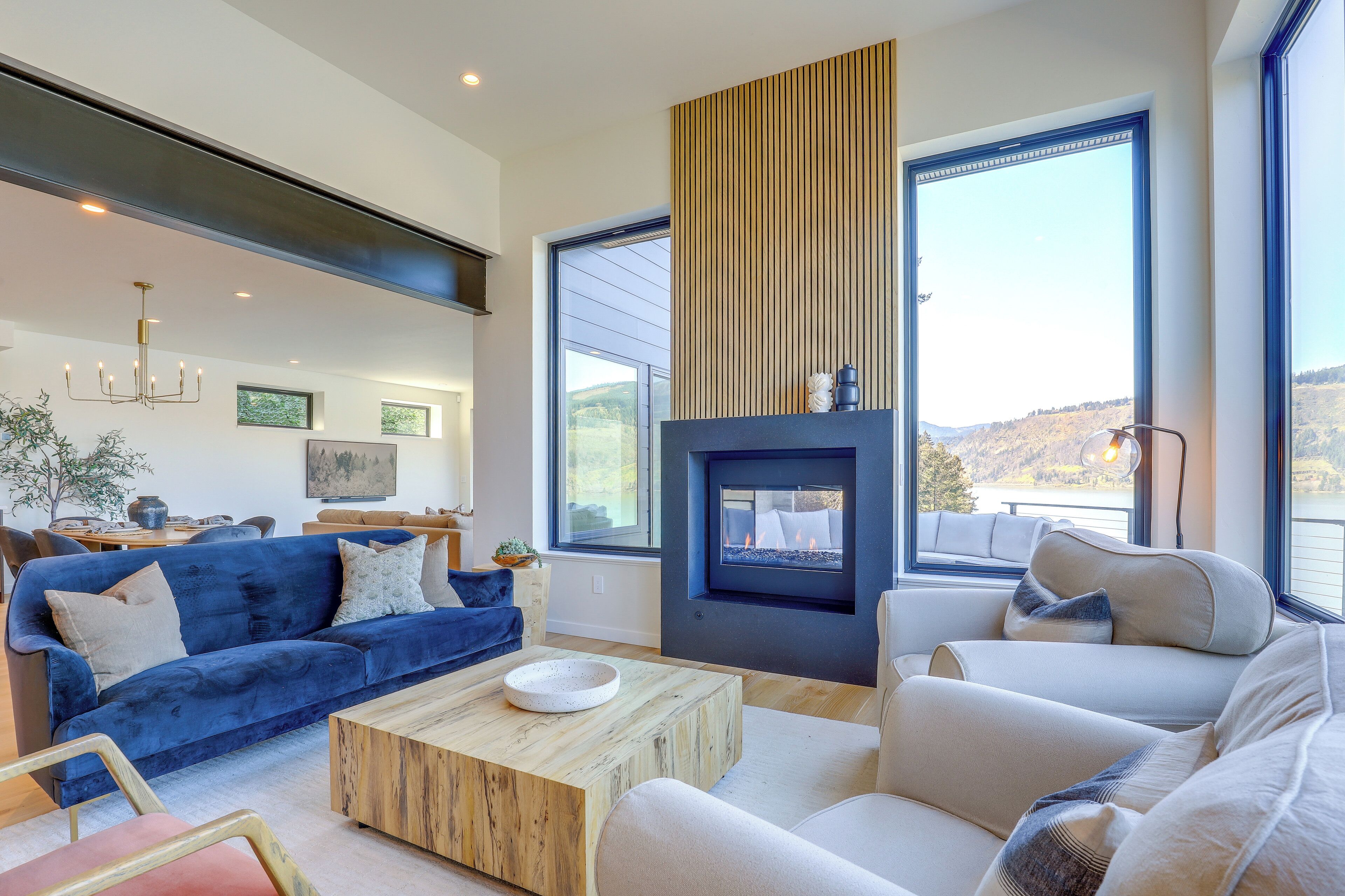 A modern living room with a fireplace, large windows, and a blue sofa.