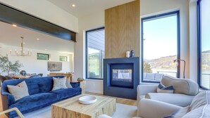 A modern living room with a fireplace, large windows, and a blue sofa.