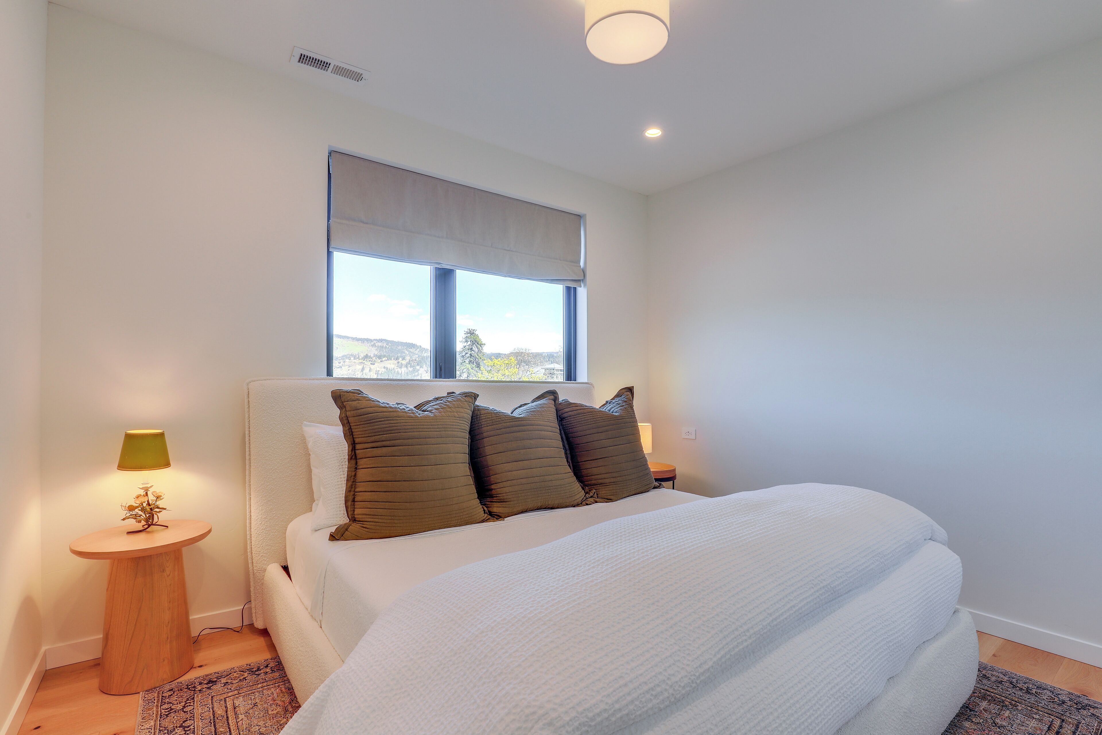 Une chambre à coucher avec un lit, une fenêtre donnant sur un beau paysage, une table de chevet avec une lampe et une petite plante décorative.