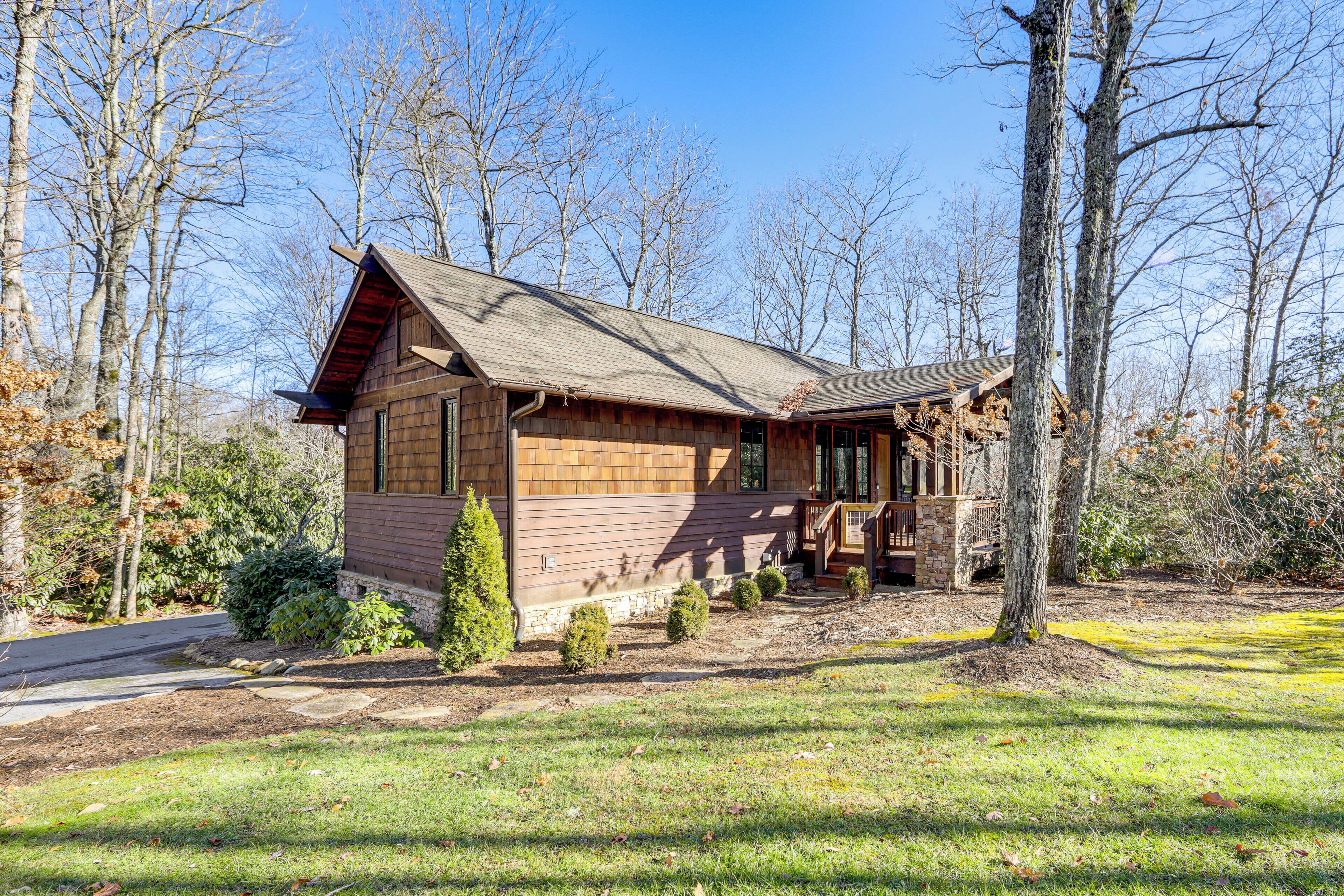 A wooden cabin with a porch, surrounded by trees and a grassy yard.