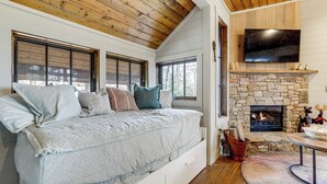 A bedroom with a bed, a stone fireplace, a TV mounted above it, and a window with blinds. - Mountain Retreat w/ Community Perks in Glenville! (Glenville)