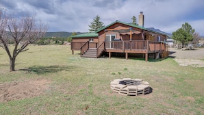 Une cabane en bois avec une terrasse, une cheminée et un foyer extérieur dans la cour.