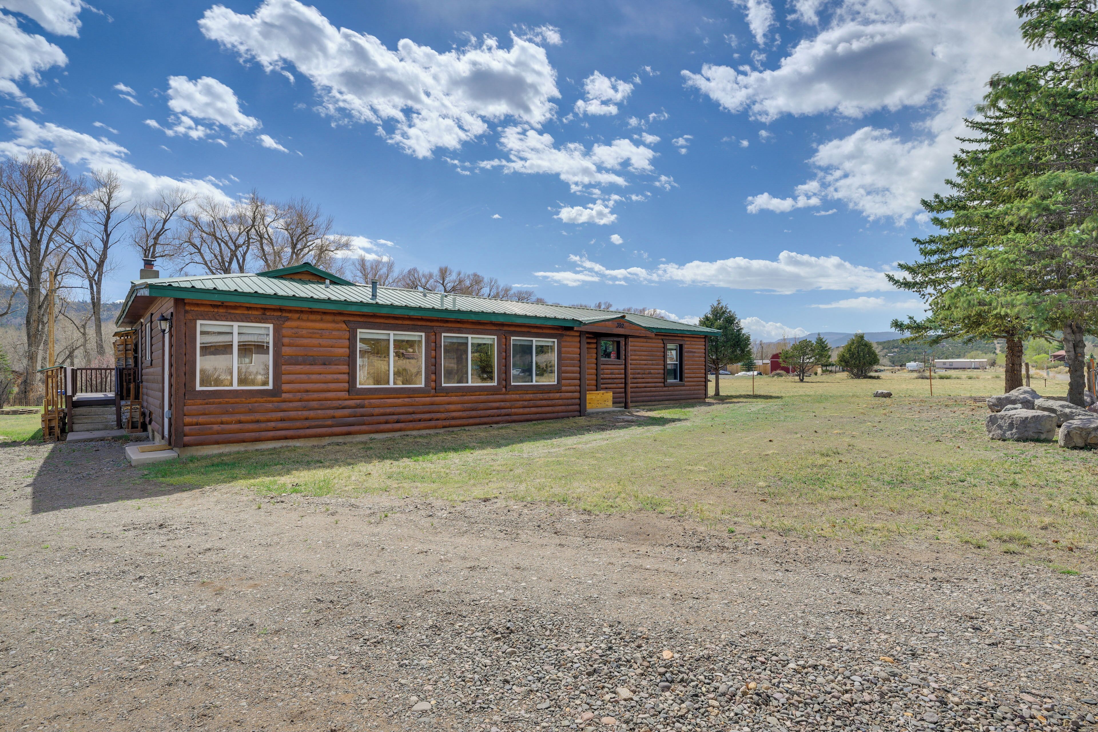A log cabin with a metal roof, a front porch, and a gravel driveway.