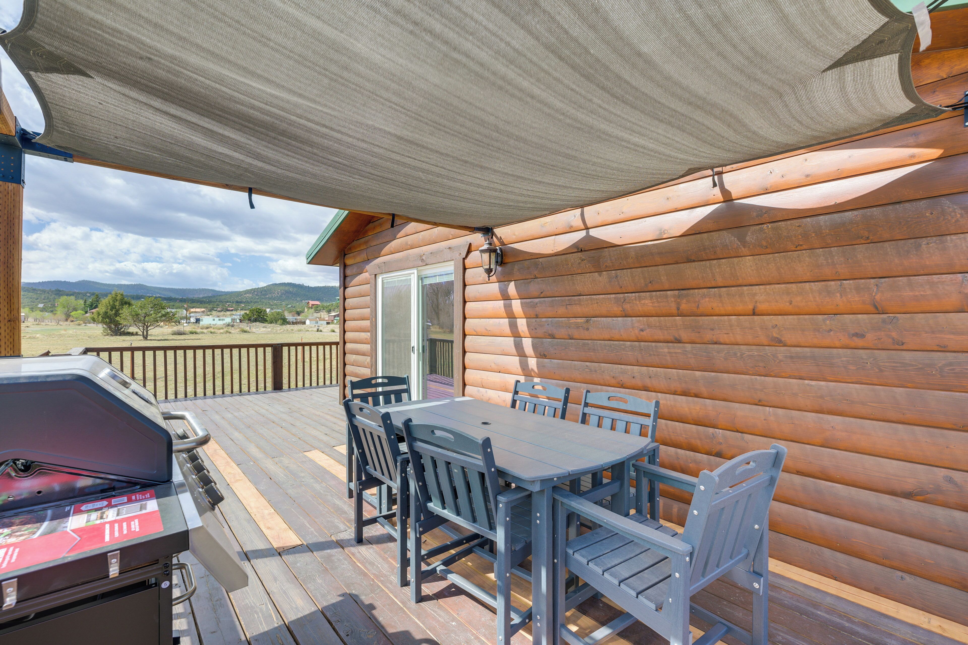 Una terraza de madera con una mesa y sillas, una parrilla y vistas del paisaje.