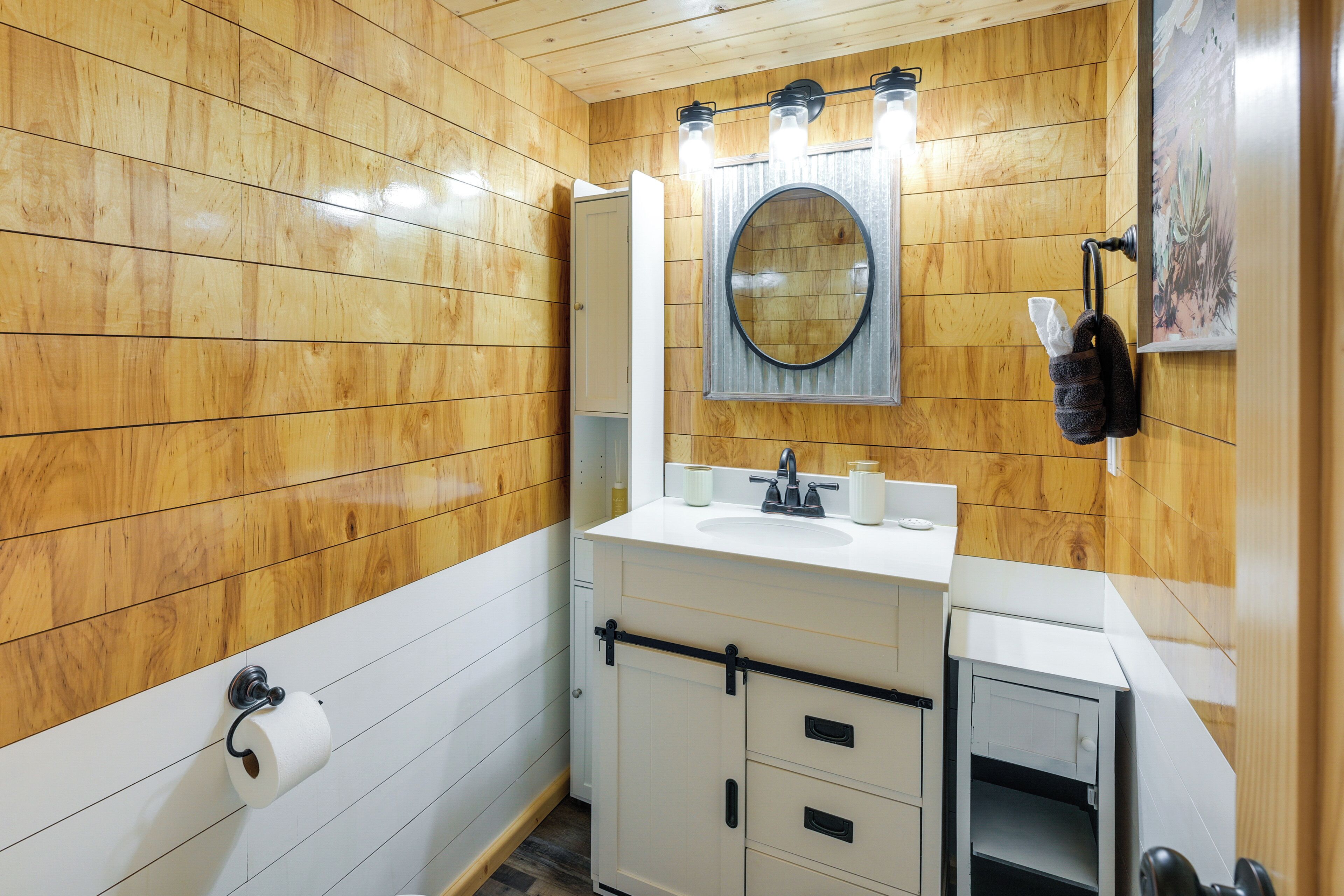 A bathroom with wooden walls, a white sink, a mirror, and a towel rack.