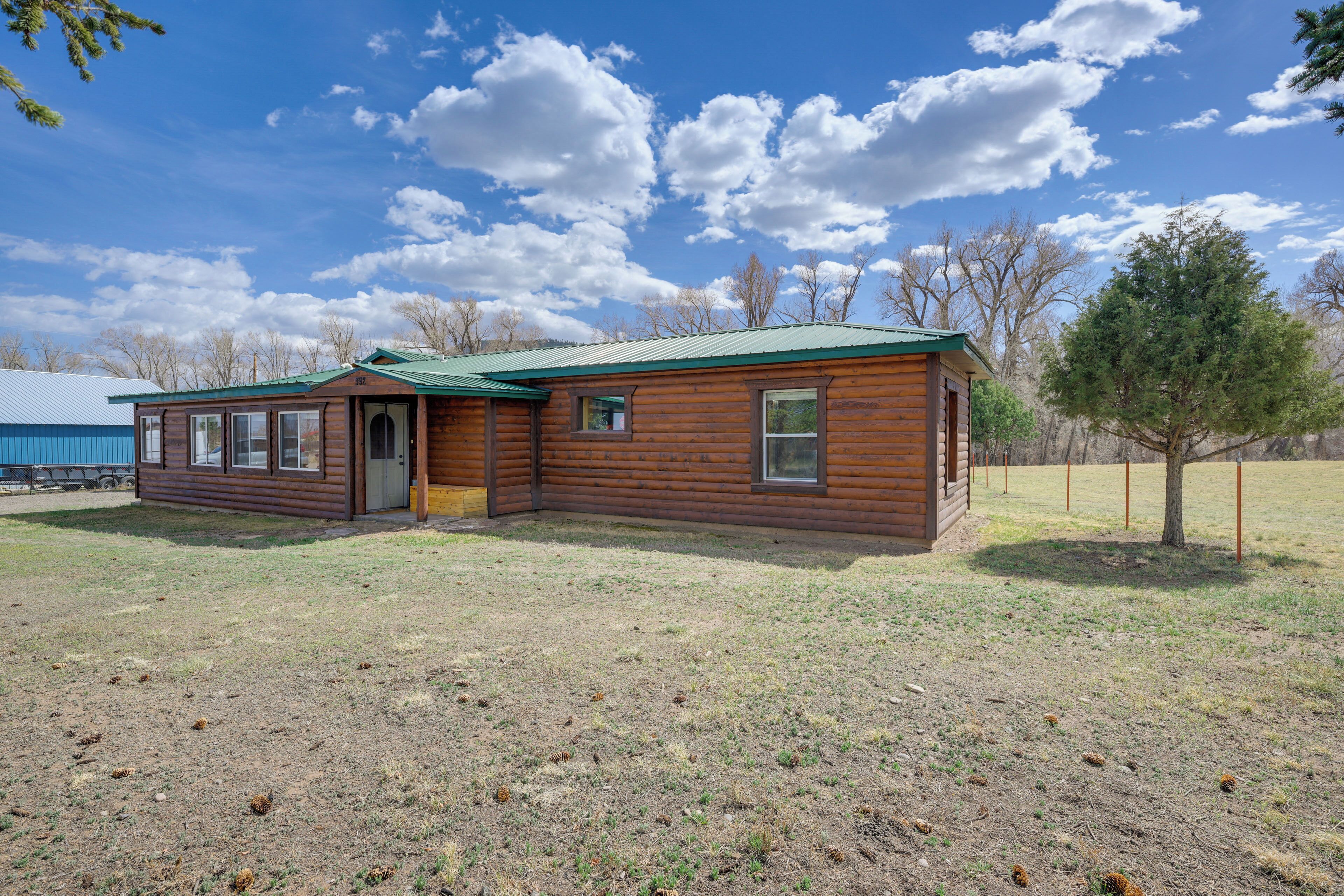 A wooden cabin with a green roof, a door, and windows, surrounded by a grassy field and trees.