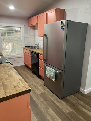 Cucina con frigorifero in acciaio inossidabile, piano di lavoro in legno e mobili arancioni.