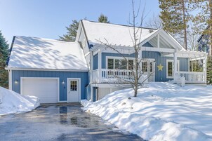Uma casa de dois andares com garagem, varanda coberta e entrada de automóveis coberta de neve.