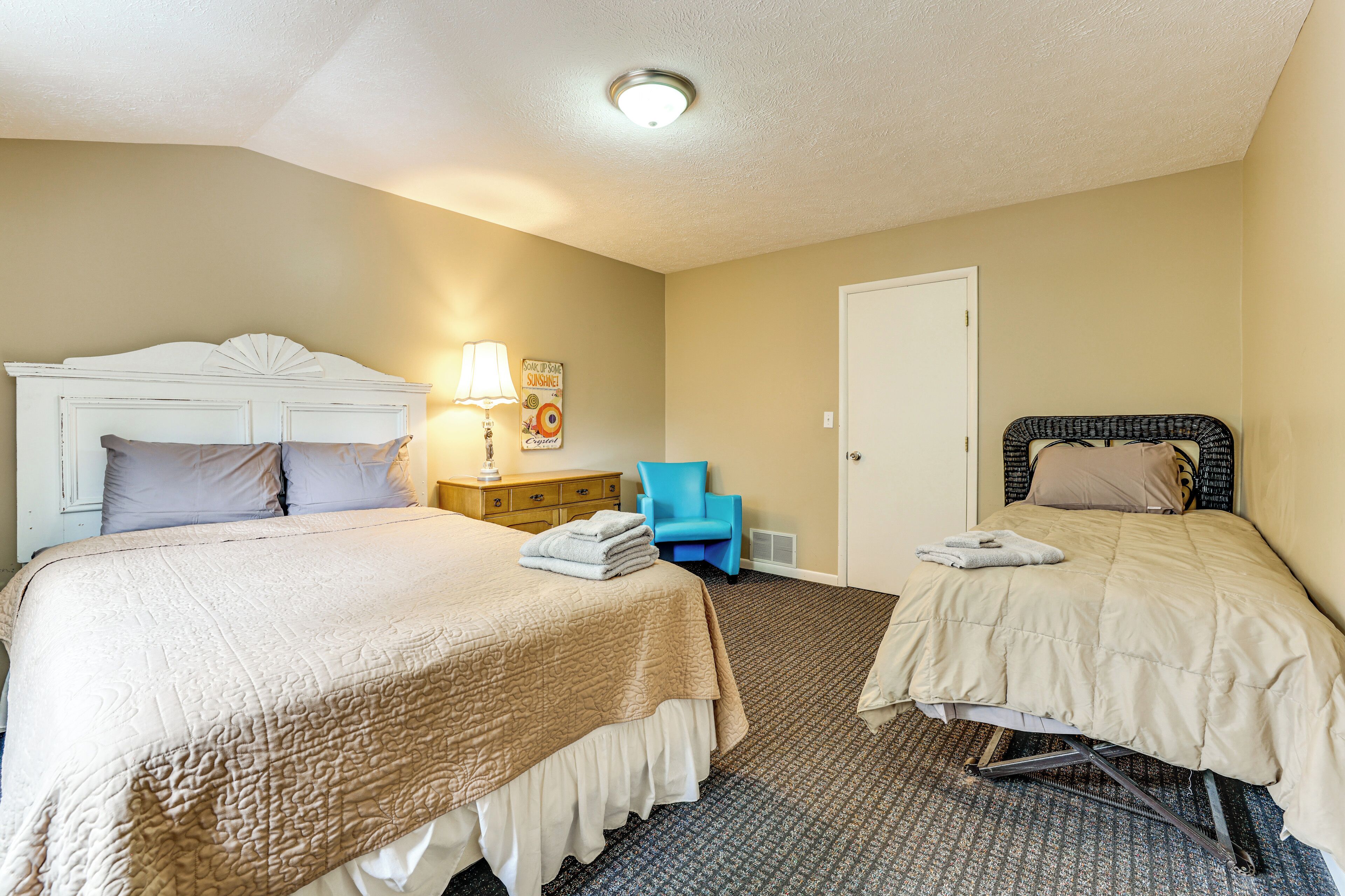 A hotel room with two beds, a chair, a nightstand, and a door.