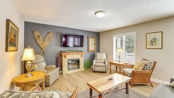 A living room with a stone fireplace, leather chairs, a television, and a large window.