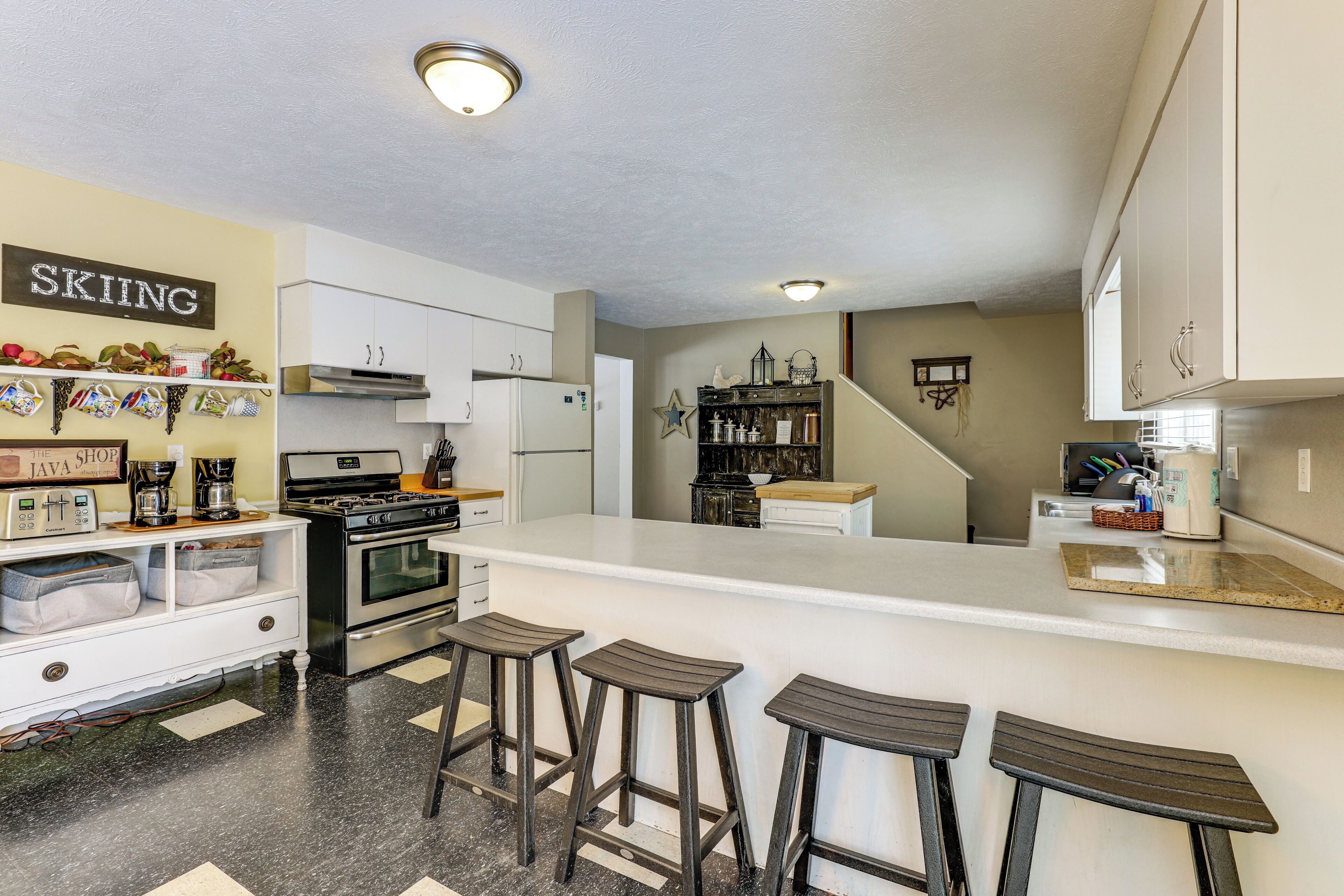 A kitchen with a bar area, white cabinets, a stove, and a coffee maker.