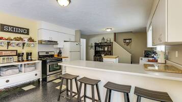 A kitchen with a bar area, white cabinets, a stove, and a coffee maker.