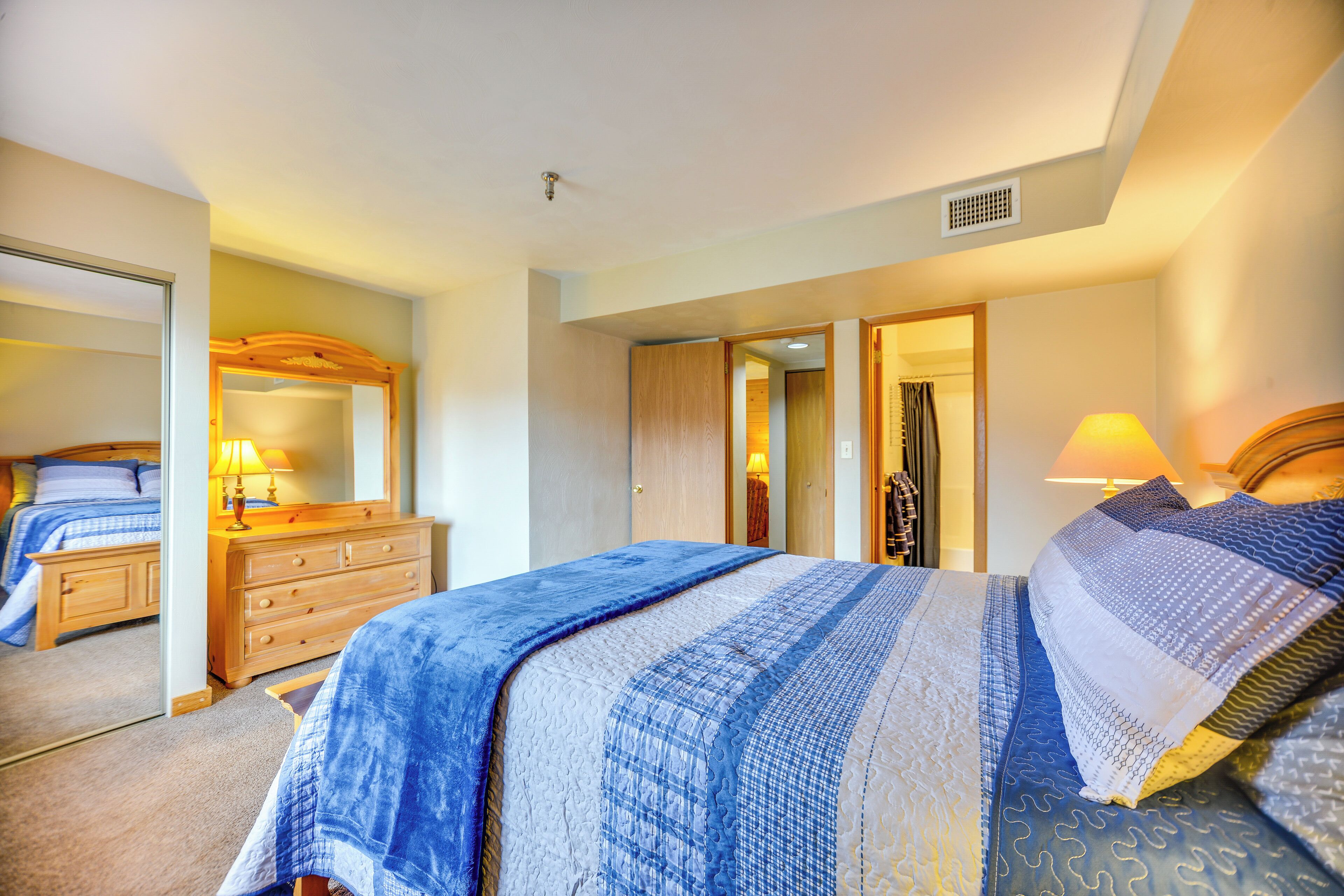 Un dormitorio con cama, cómoda, espejo y puerta que da a otra habitación.