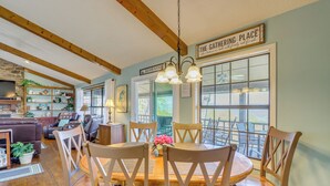 Un comedor con una mesa y sillas de madera, un candelabro y vistas amplias a través de ventanas grandes.