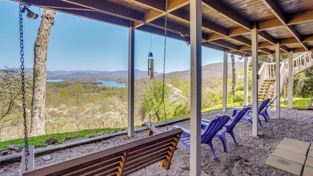 Un área de estar al aire libre con techo, con un banco y sillas, con vistas a un paisaje pintoresco de montañas y un lago.
