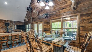 A rustic dining area with wooden chairs, a glass table, and a view of the outdoors through large windows. - Lake Barkley Fishing Getaway w/ Private Dock! (Cadiz)