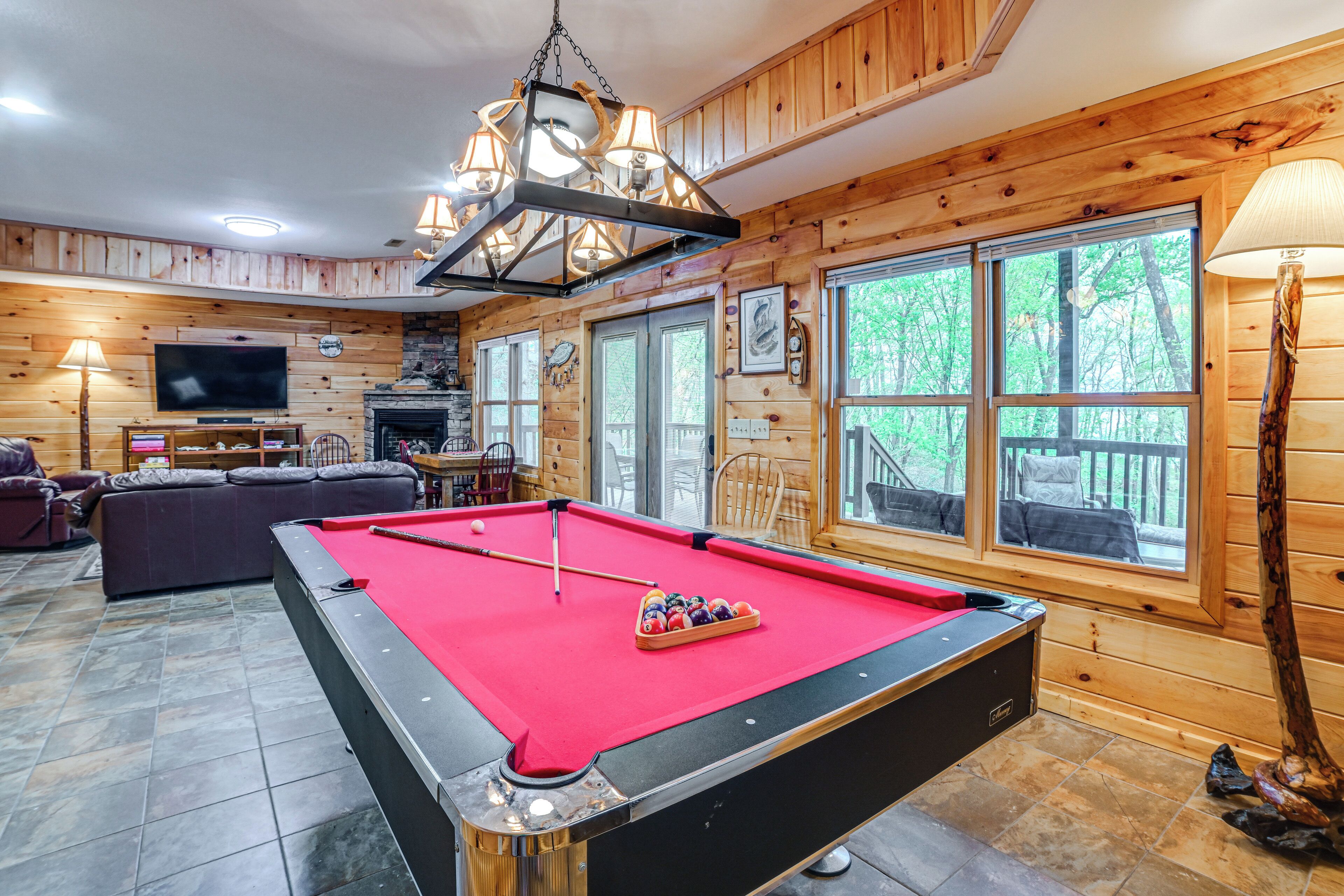 A pool table in a room with wooden walls, a television, and a fireplace.