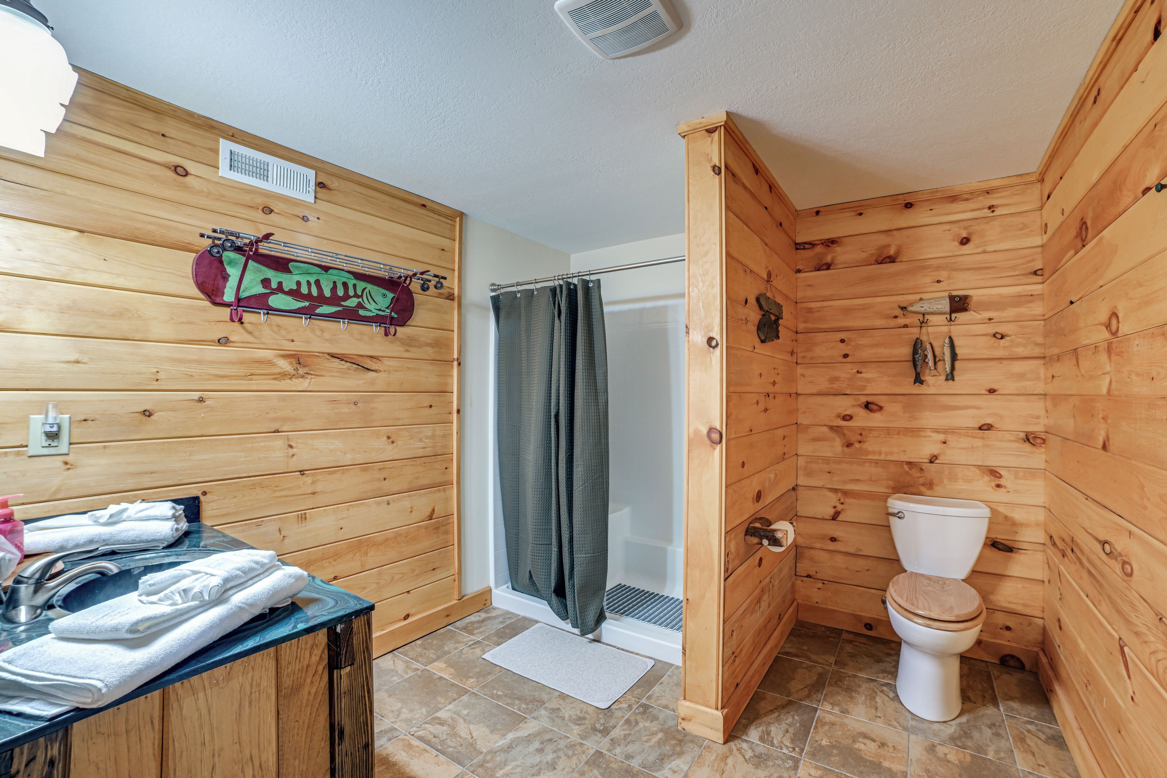 Une salle de bain rustique, aménagée dans une cabane en bois, avec une douche, des toilettes et un porte-serviettes avec des serviettes.