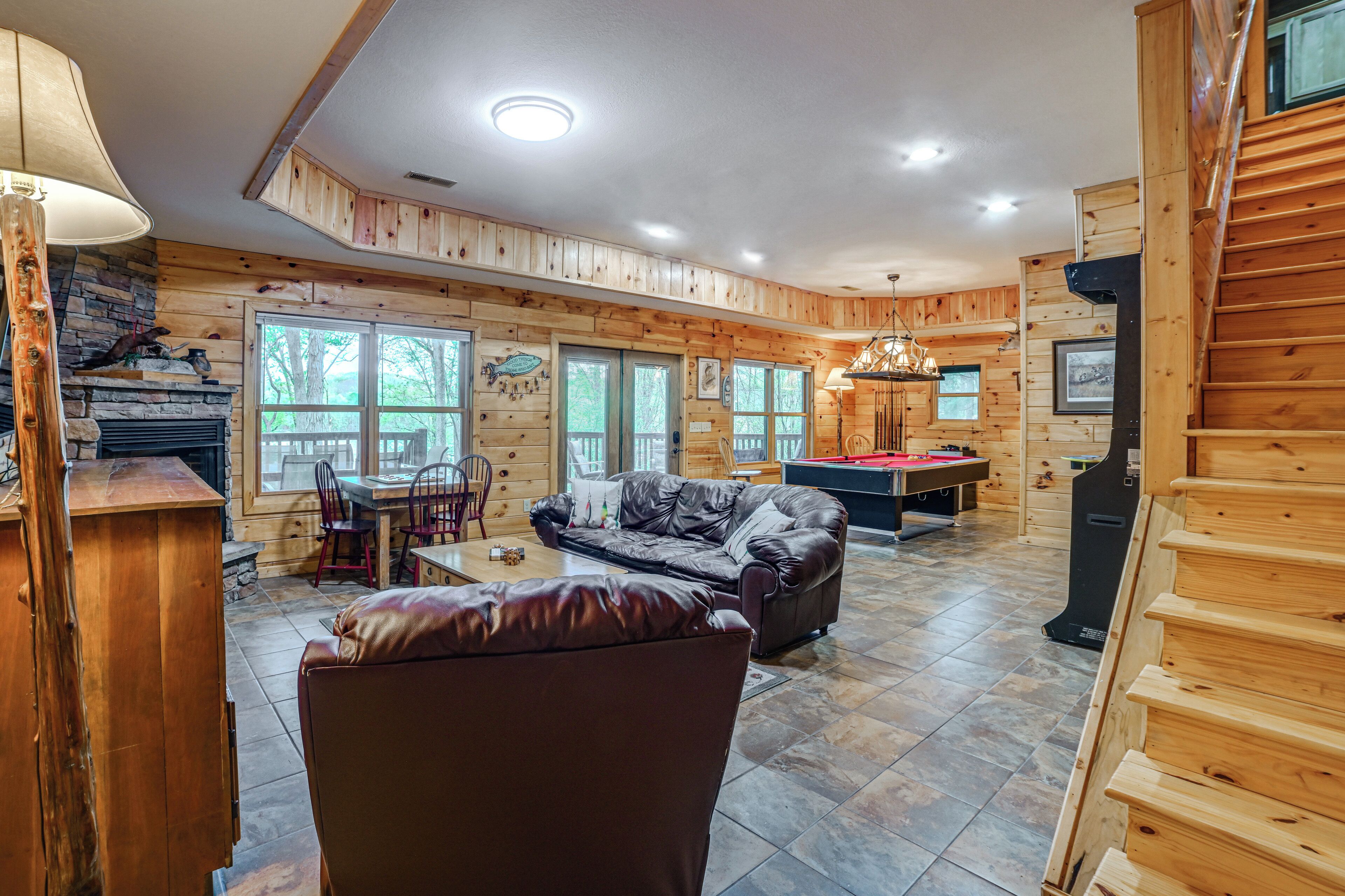 A log cabin interior with a fireplace, wooden walls, a billiards table, and a leather sofa.