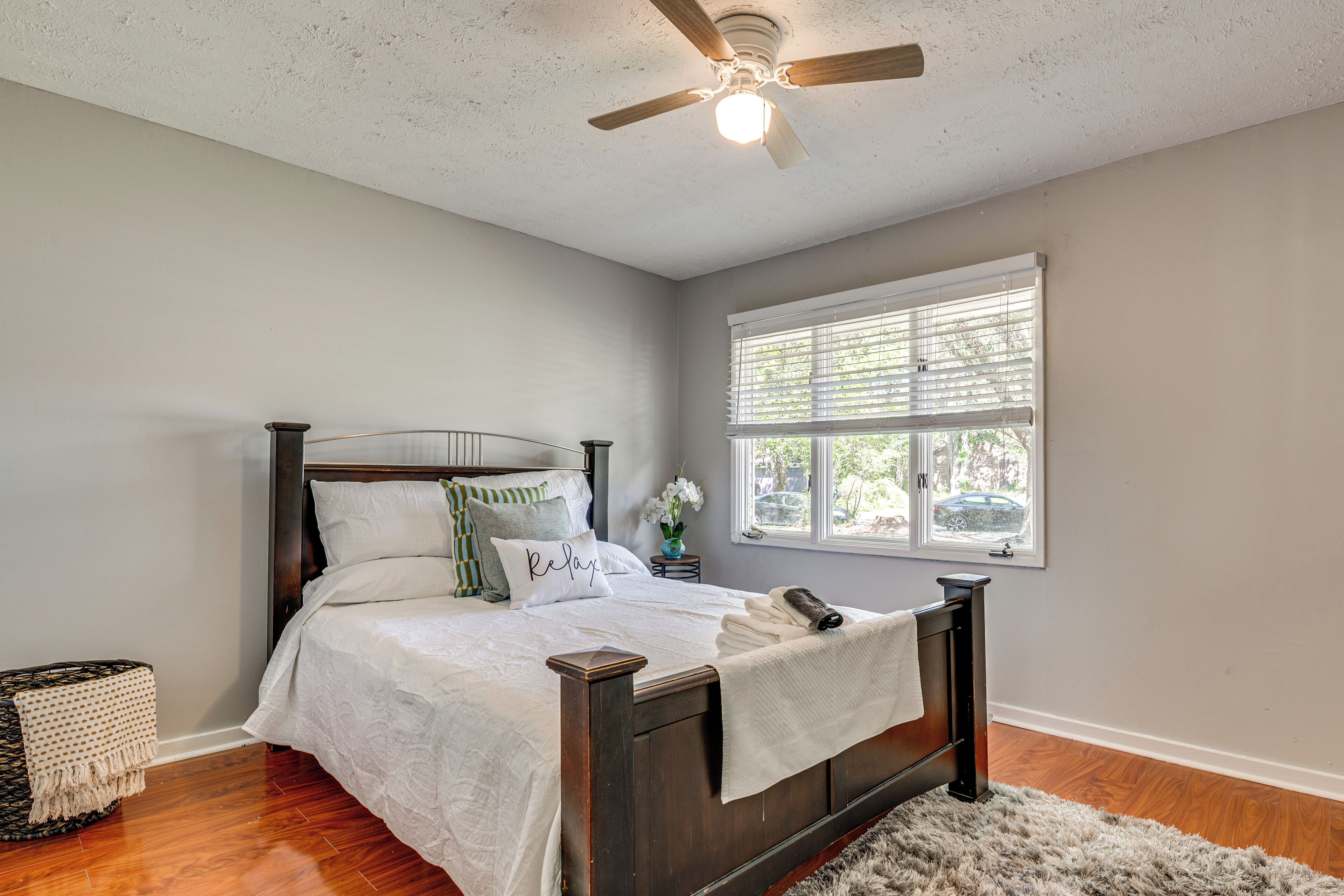Une chambre à coucher avec un lit, un ventilateur de plafond, une fenêtre avec des stores et une petite table de chevet sur laquelle se trouve un vase.