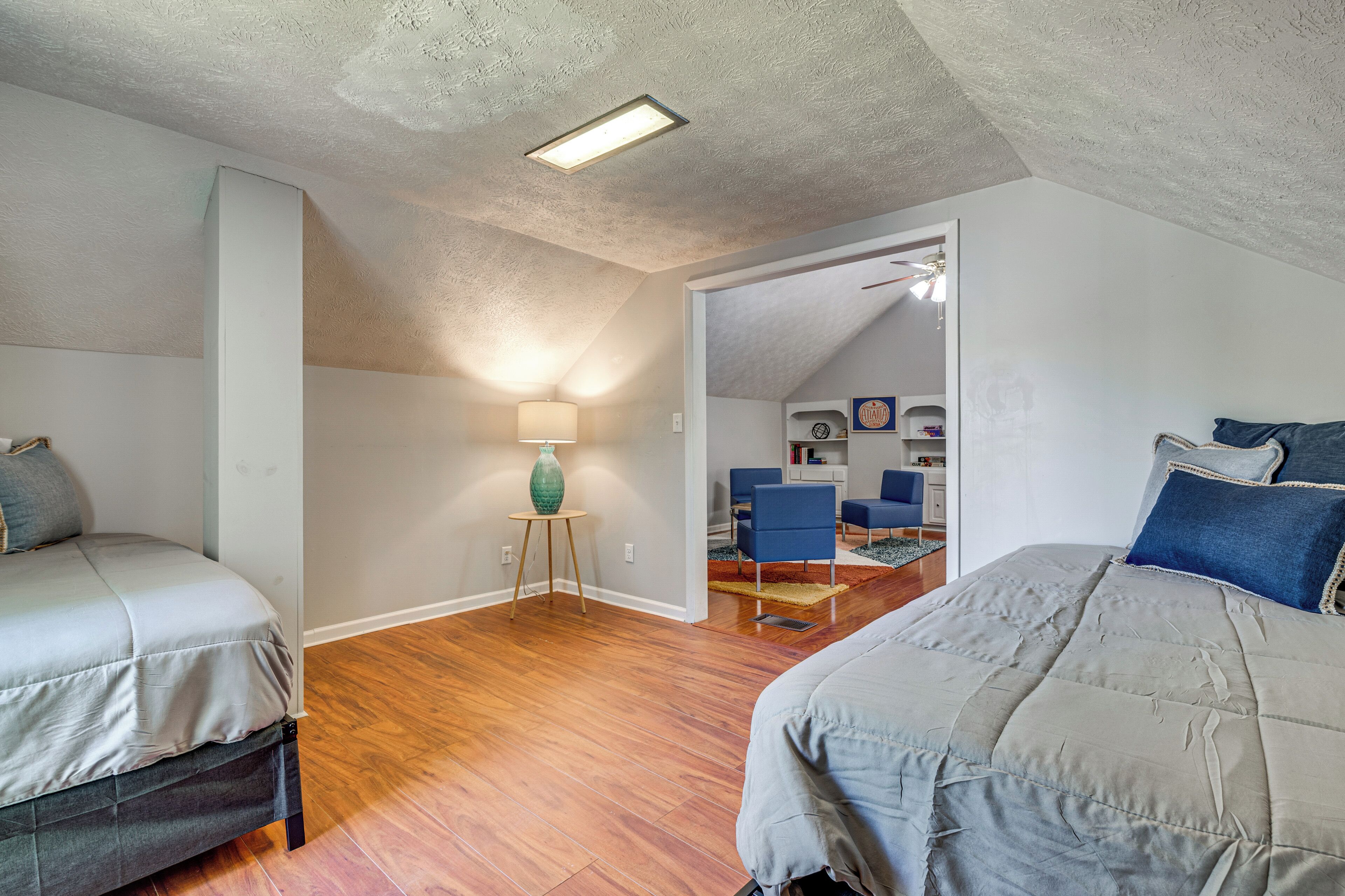 A bedroom with two beds, a lamp, and a view into another room.