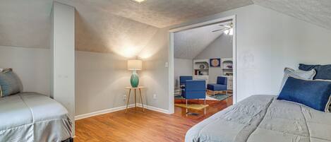 A bedroom with two beds, a lamp, and a view into another room.