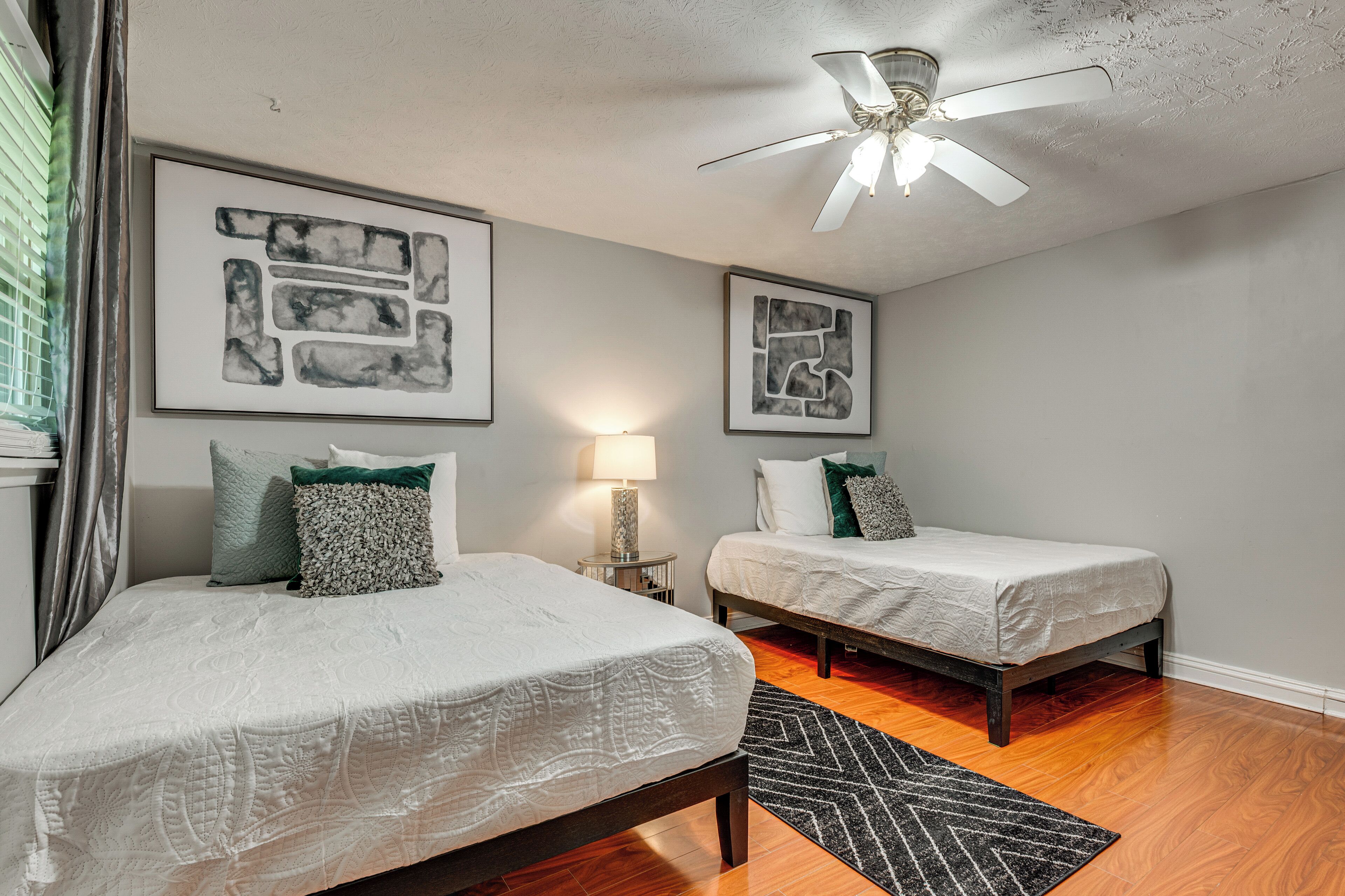 A bedroom with two beds, a ceiling fan, and artwork on the walls.