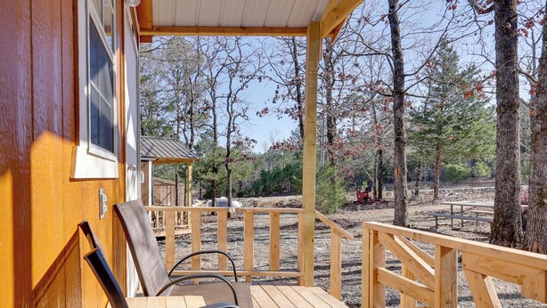Une terrasse en bois, avec des chaises et une table, donnant sur une zone boisée avec des arbres et une table de pique-nique.