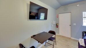 A room with a flat-screen TV mounted on the wall, a foldable table with chairs, a door, and a window. - Small Family Getaway in Mena w/ Trails On-site! (Mena)