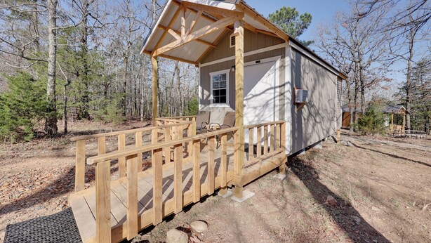 A small cabin with a wooden porch and a covered entryway, surrounded by trees. - Small Family Getaway in Mena w/ Trails On-site! (Mena)