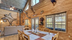Interior rústico de una cabaña con comedor de madera, monturas de animales en la pared y un gran cuero de piel.