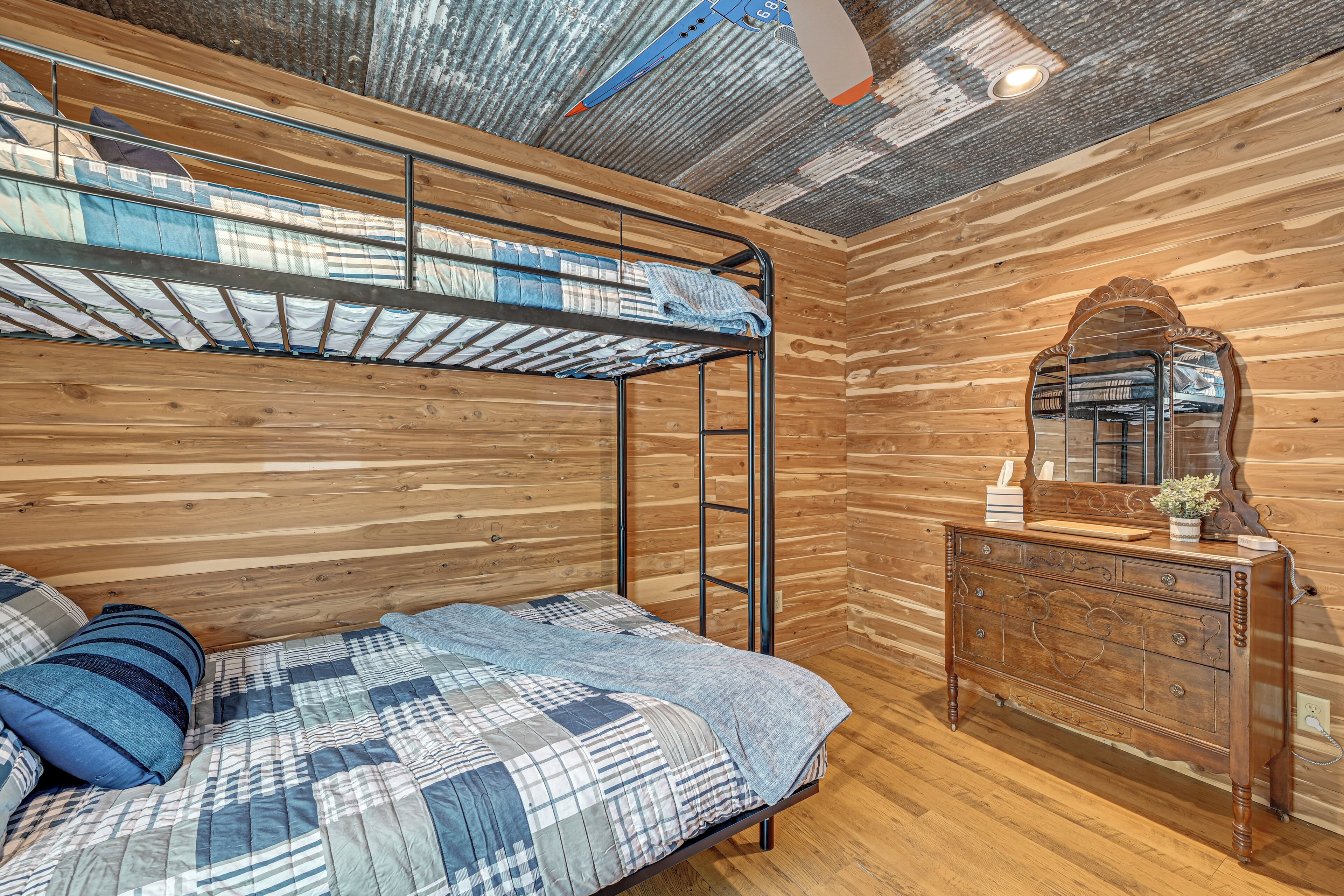 En køjeseng med trægavl, en kommode med spejl og et loft med bølget metaldesign.