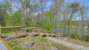 Un muelle de madera que conduce a un lago, rodeado de árboles y terreno rocoso.