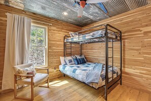 A bunk bed room with wooden walls, a window with curtains, a chair, and a ceiling fan. - Group Escape 3 Mi to Nolin Lake! Fish, Hike & Boat (Cub Run)