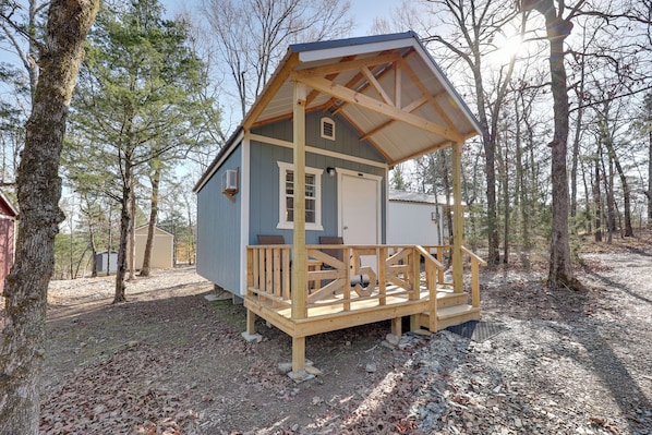 A small cabin with a wooden deck, a garage, and a covered porch. - Quiet & Cozy Ouachitas Mtns Cabin w/ Trail Access (Mena)