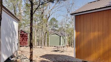 A wooden shed with a bench and a table in a wooded area.