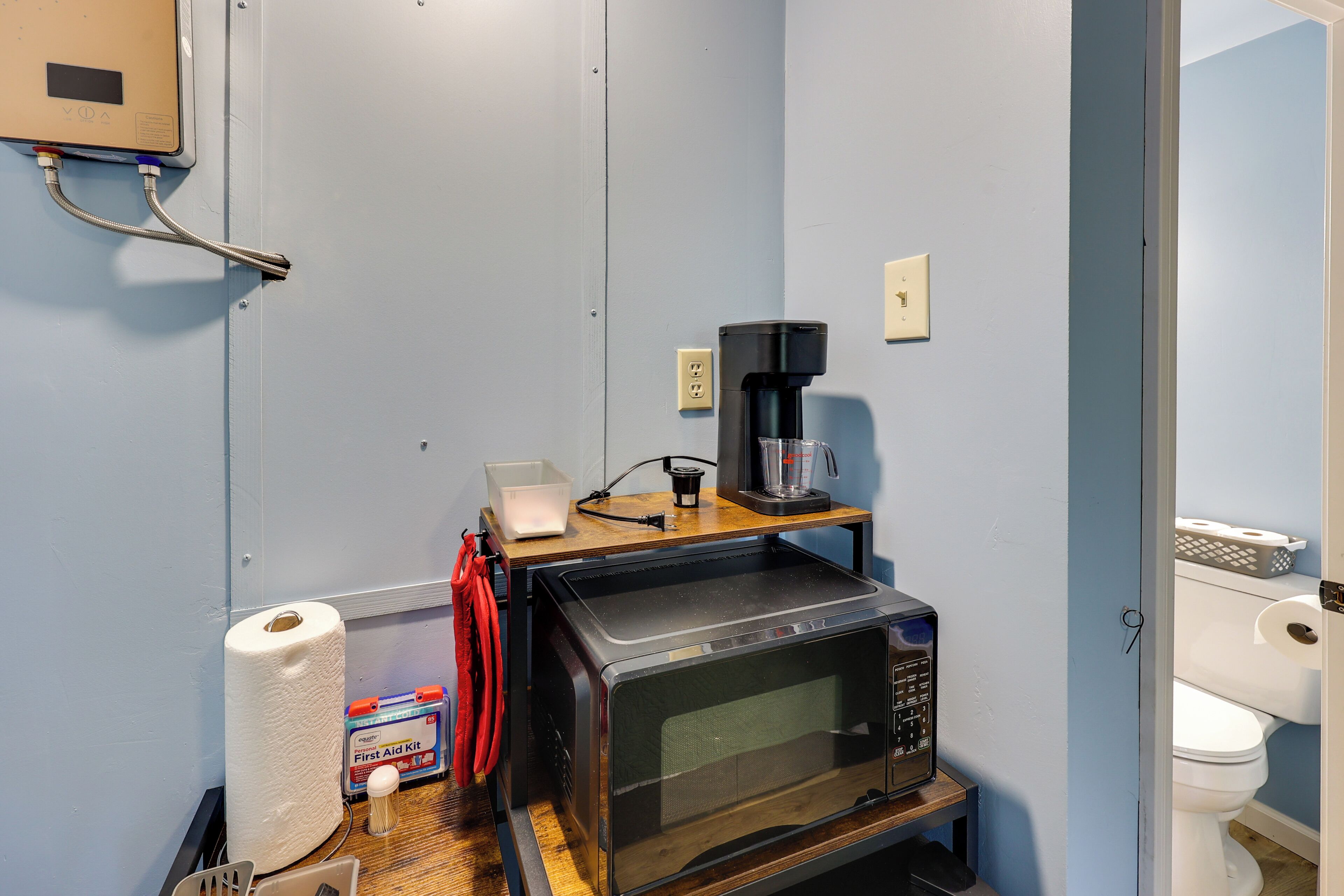 A compact kitchenette with a microwave, coffee maker, and a small shelf with a box of tissues.