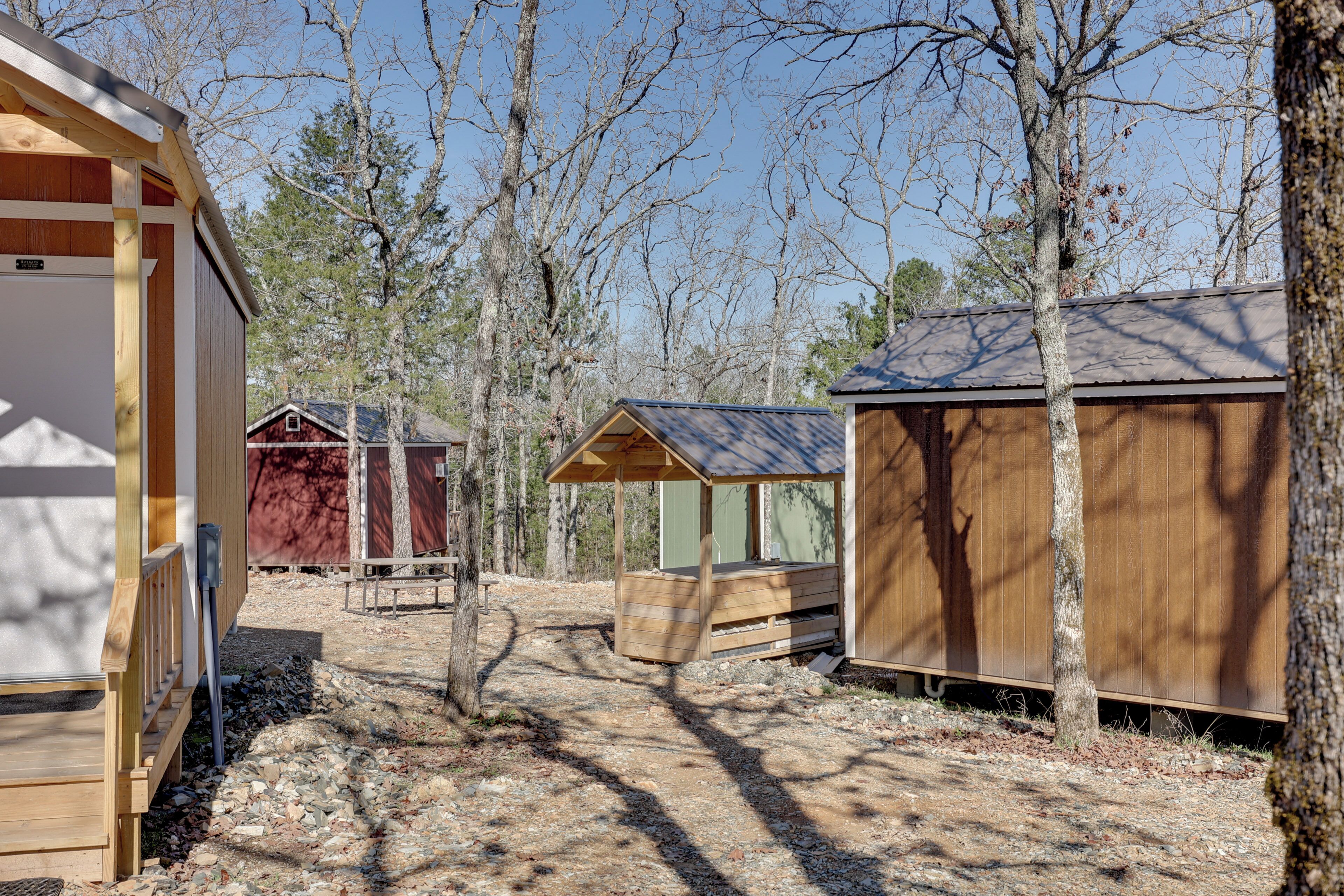A rustic cabin area with wooden structures, a gravel path, and surrounding trees.