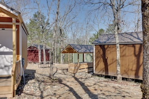 A rustic cabin area with wooden structures, a gravel path, and surrounding trees. - Gem Mine & Hike! Unique Stay in Ouachita Mountains (Mena)
