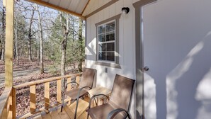 Una terraza de madera con dos sillas y una mesa, una puerta blanca y una ventana con persianas.