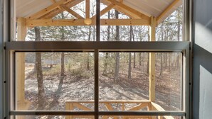 Una cabaña de madera con un ventanal grande, una terraza de madera y vistas al bosque.