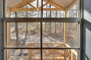 A wooden cabin with a large window, a wooden deck, and a forest view.