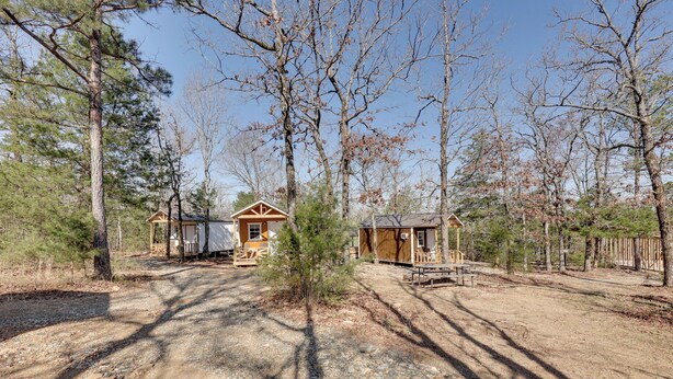 Una cabaña rústica con un sendero de tierra que la conduce, rodeada de árboles y una valla de madera.