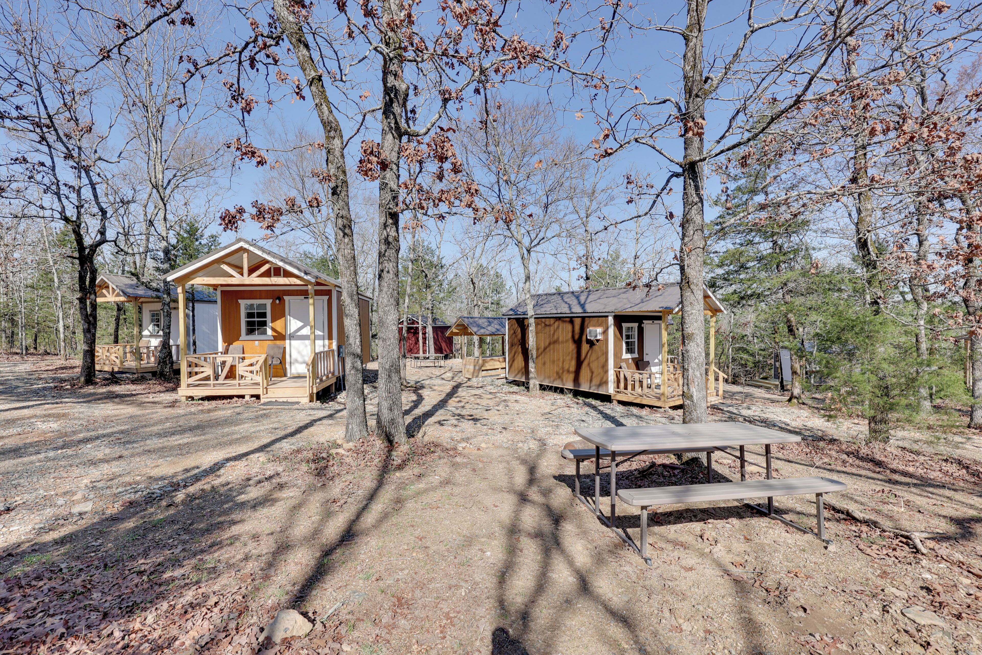 A campsite with wooden cabins, picnic tables, and trees.
