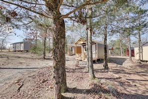 A rustic cabin with a wooden deck, surrounded by trees and a dirt ground.