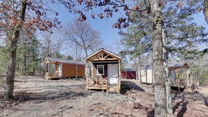 A rustic cabin with a porch, surrounded by trees and other cabins. - Ouachitas Adventure Base! Charming Tiny Cabin (Mena)