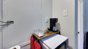 A small kitchenette with a microwave, coffee maker, and a clear plastic container on a wooden countertop. - Ouachitas Adventure Base! Charming Tiny Cabin (Mena)