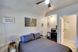 A bedroom with a bed, a ceiling fan, a painting, a desk with a computer, and a microwave.