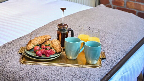 A neatly made bed with a breakfast tray, a brick wall, and a small table with a lamp and plant. - Stylish 2BR Home | Central Hebden Bridge Escape (Hebden Bridge)